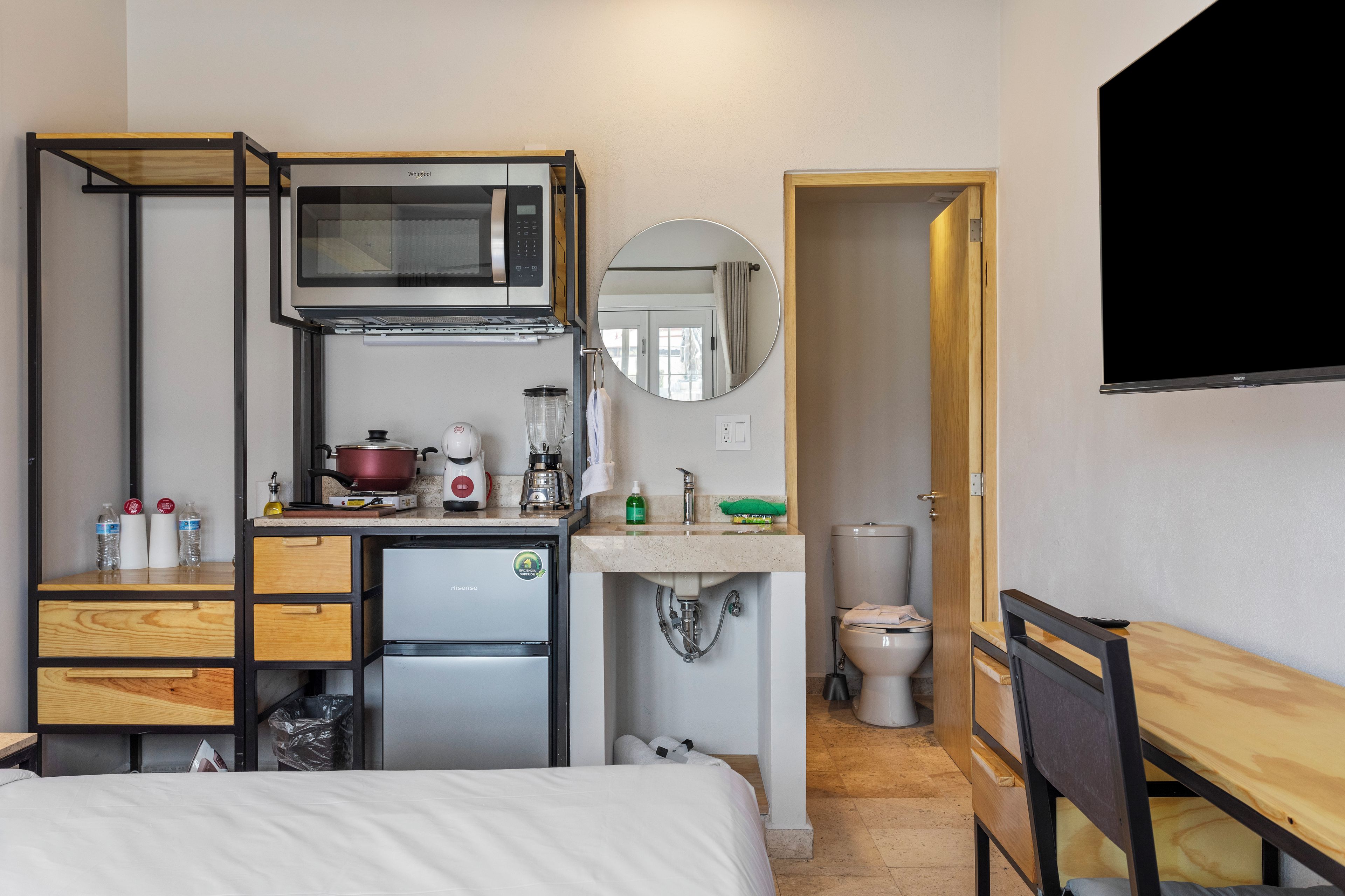 A compact hotel room with a kitchenette, a bed, a desk, and a bathroom.