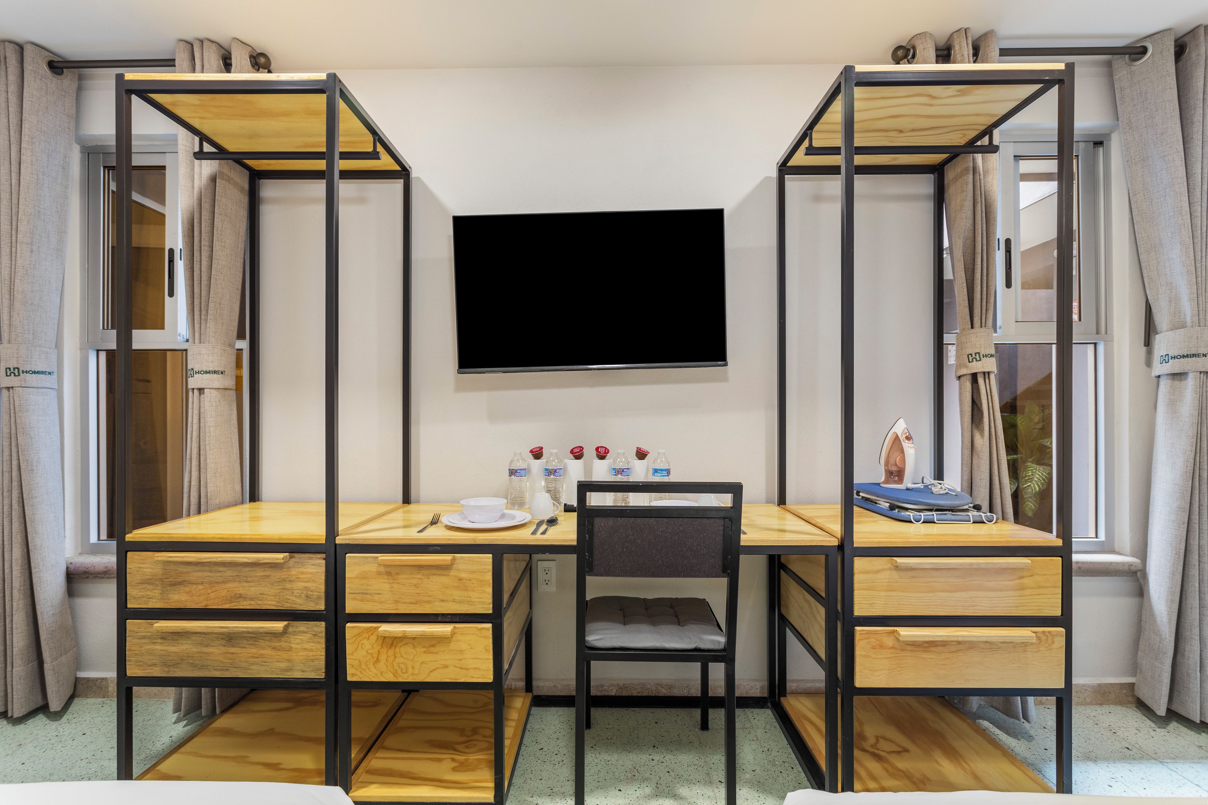 A room with a bunk bed, a desk with a chair, a television, and a small ironing board.