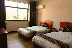 Habitación de hotel con dos camas, ventana, aire acondicionado y piso de madera.