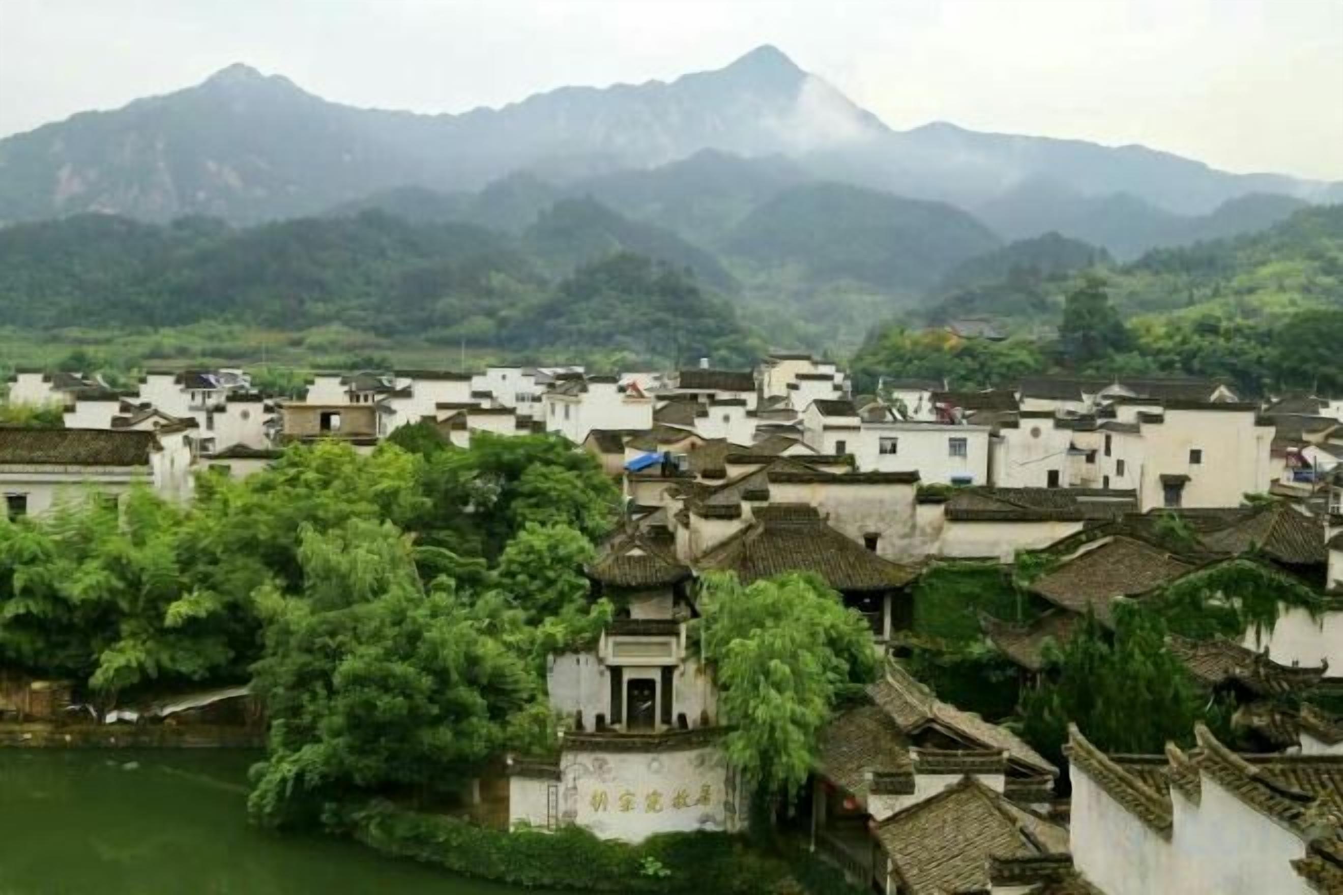 Un pueblo tradicional con edificios blancos, un río y montañas al fondo.