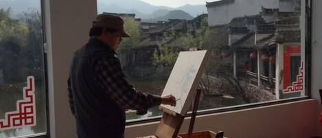 Una persona dipinge a una finestra con vista sull'architettura tradizionale.