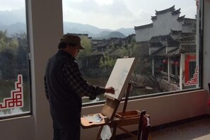 Una persona pinta frente a una ventana con vistas a la arquitectura tradicional.