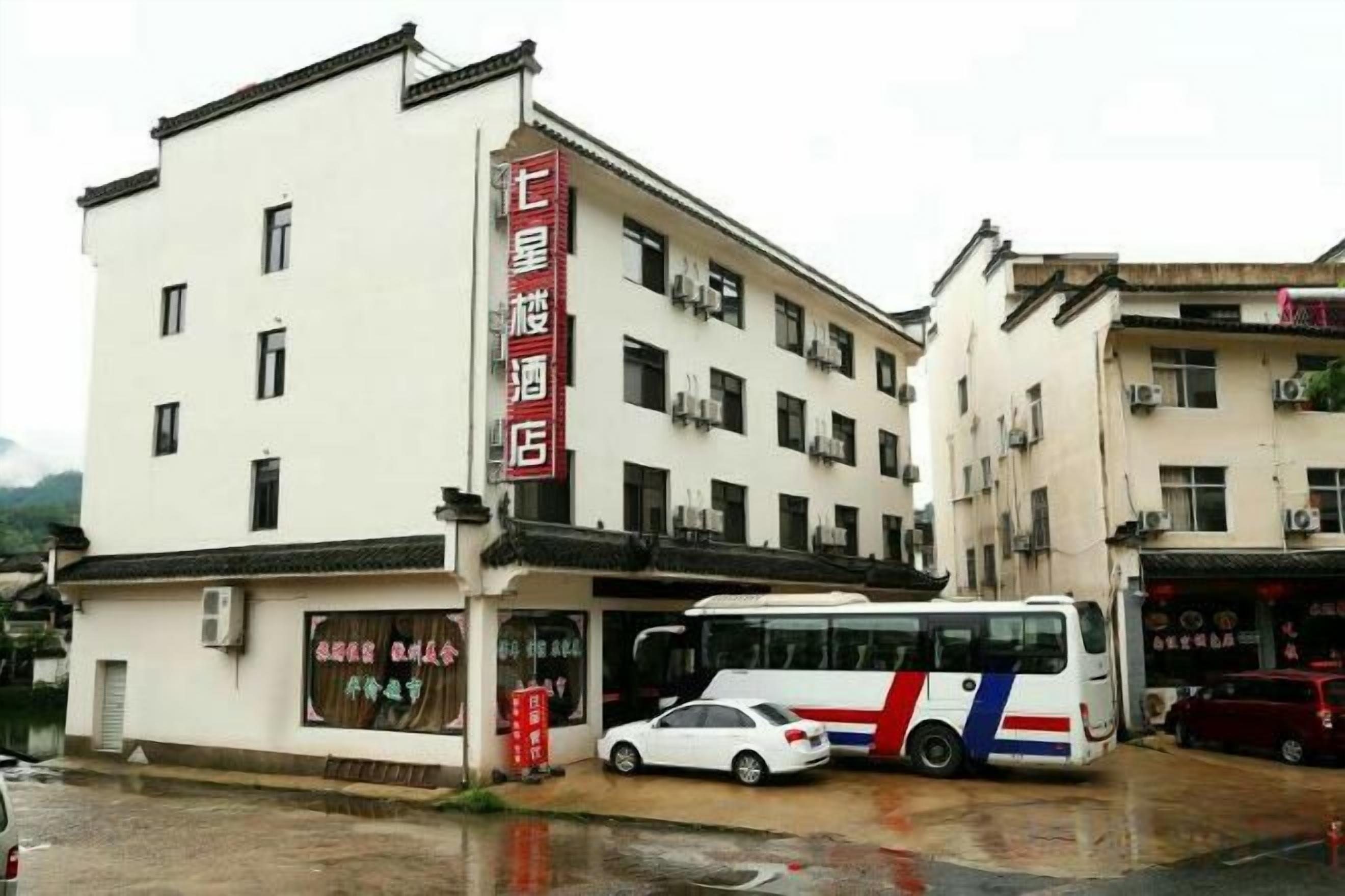 A hotel with a red sign, a parked bus, and a car in front.