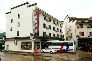 Un hotel con un letrero rojo, un autobús estacionado y un coche en la entrada.