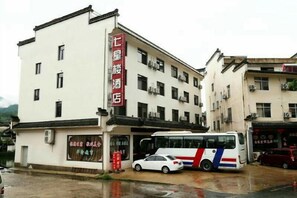 Un hotel con un letrero rojo, un autobús estacionado y un coche en la entrada.