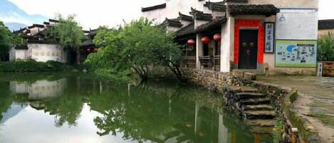 A traditional building with a red door, adjacent to a calm water body, reflecting the structure.