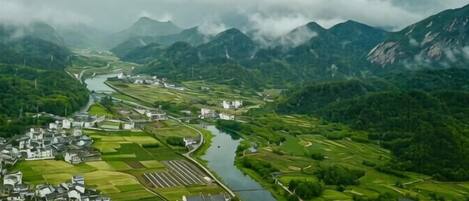 A river flowing through a valley with a town on one side and mountains in the background.