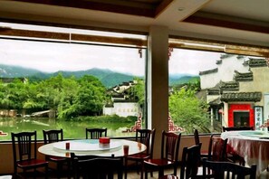 Comedor con una mesa redonda y sillas, ventanas amplias con vista a un río y edificios tradicionales.