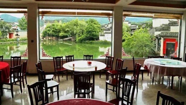 Un espace repas avec des tables et des chaises rondes, de grandes fenêtres offrant une vue sur un lac et des bâtiments traditionnels.