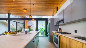 Une cuisine moderne dotée d’un grand îlot central, d’un plafond en bois et donnant sur un espace extérieur.