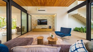 Un salon moderne avec un plafond en bois, une grande télévision, un fauteuil bleu et un escalier menant à un espace extérieur.