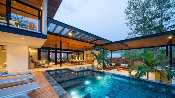 Un espace piscine extérieur moderne, doté d’une terrasse en bois, de chaises longues et d’un coin repas.