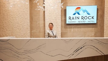 A reception desk at Rain Rock Casino, Resort & Hotel with a marble design and a logo on the wall.