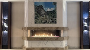 A modern fireplace with a built-in TV screen above it, set in a spacious lobby with marble walls and a large stone-tiled floor.