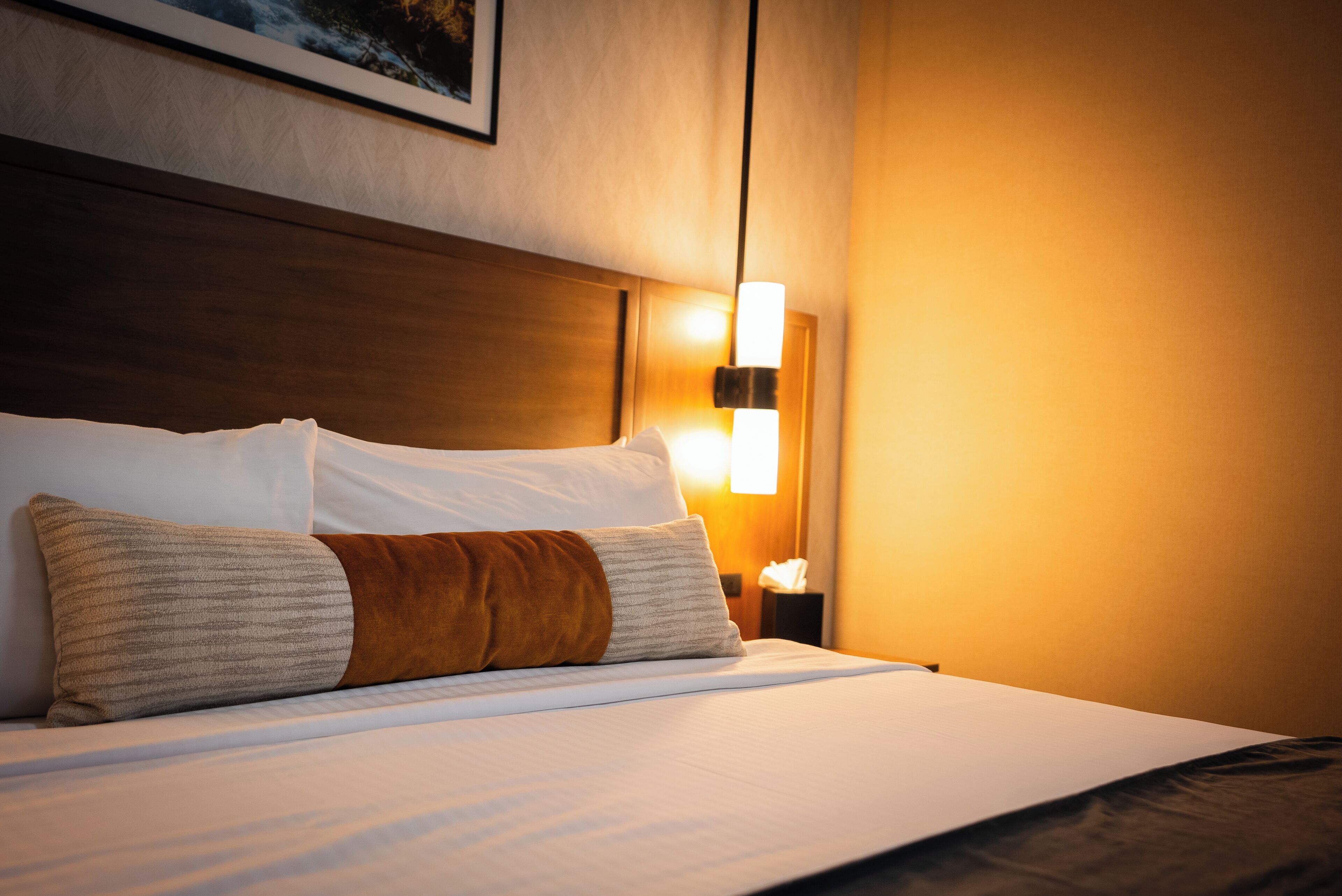Un lit bien fait, avec des draps blancs et deux oreillers, une tête de lit en bois et une lampe de chevet.