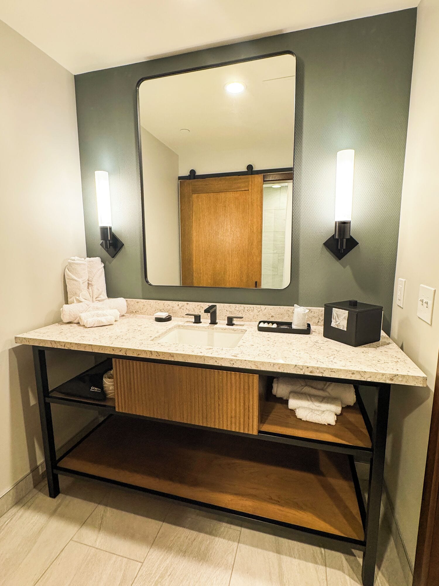 A bathroom with a double sink, a large mirror, two wall-mounted lights, and a wooden vanity.