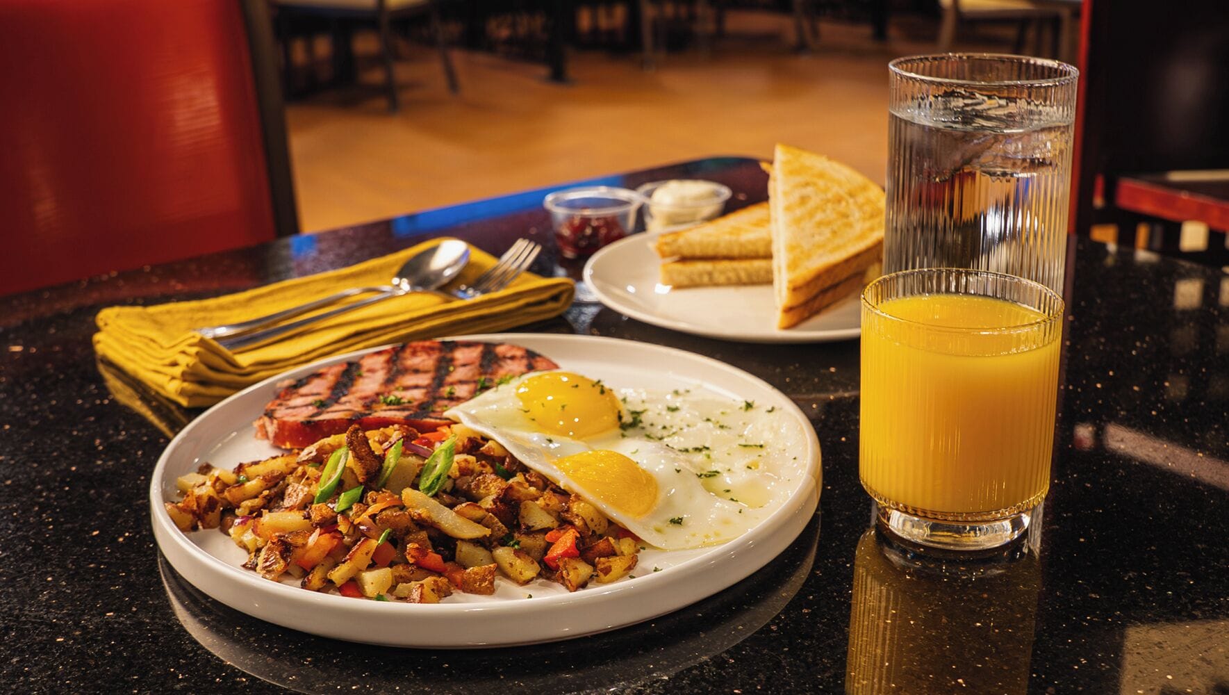 A breakfast plate with scrambled eggs, sautéed vegetables, and a grilled steak, accompanied by toast and a glass of orange juice.