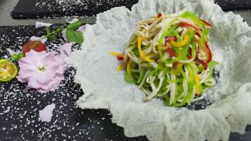 Ensalada en un tazón texturizado sobre una superficie oscura, con pétalos de flores esparcidos y una rodaja de limón.