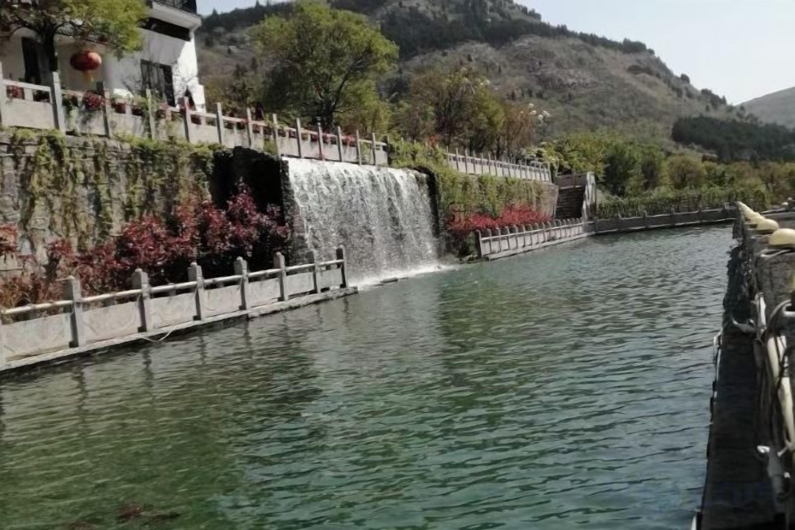 Un río tranquilo con cascada, un puente y un edificio de fachada blanca.
