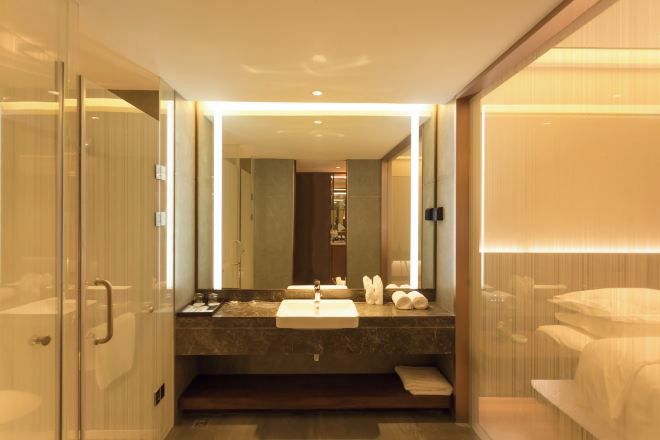 Un baño moderno con cabina de ducha de vidrio, un espejo grande, encimera de mármol y inodoro empotrado.