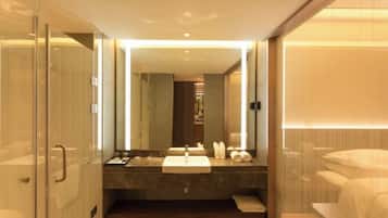 Un baño moderno con cabina de ducha de vidrio, un espejo grande, encimera de mármol y inodoro empotrado.