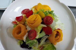 Un plato blanco con una ensalada de lechuga, tomates y pimientos amarillos.