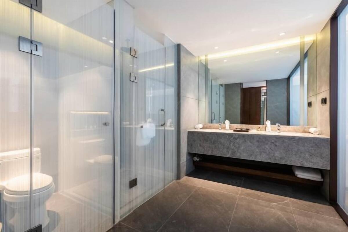 Un baño moderno con ducha de vidrio, tocador de mármol y un espejo grande.