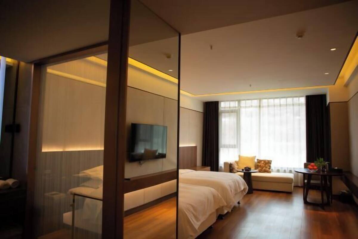 Una habitación de hotel moderna con una cama grande, televisión, zona de estar y vistas al exterior.