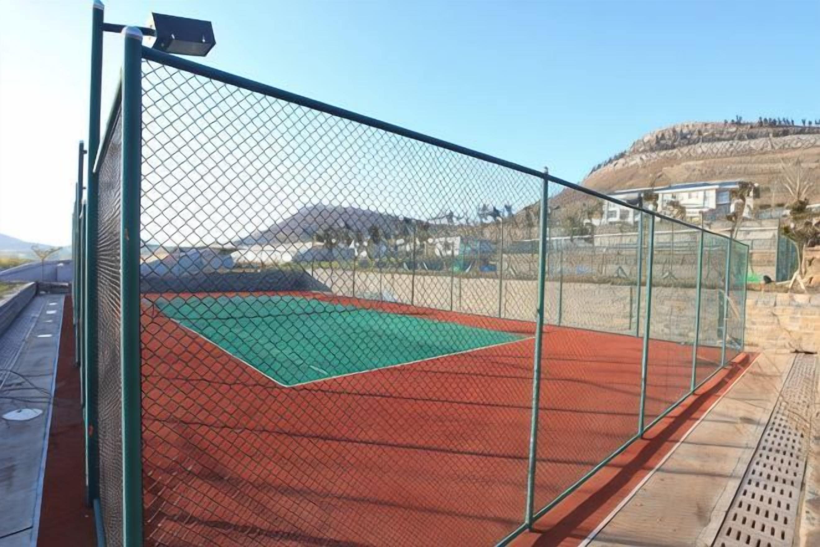 Cancha de tenis rodeada por una valla, con superficie de juego verde y borde rojo.