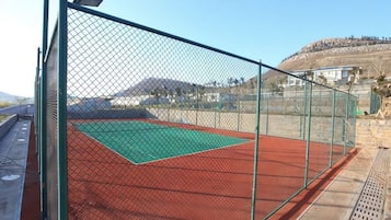 Cancha de tenis rodeada por una valla, con superficie de juego verde y borde rojo.