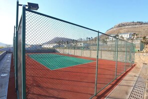 Cancha de tenis rodeada por una valla, con superficie de juego verde y borde rojo.