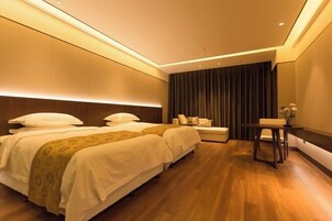 A hotel room with two beds, a bedside table, a small seating area, and a dark curtain backdrop.