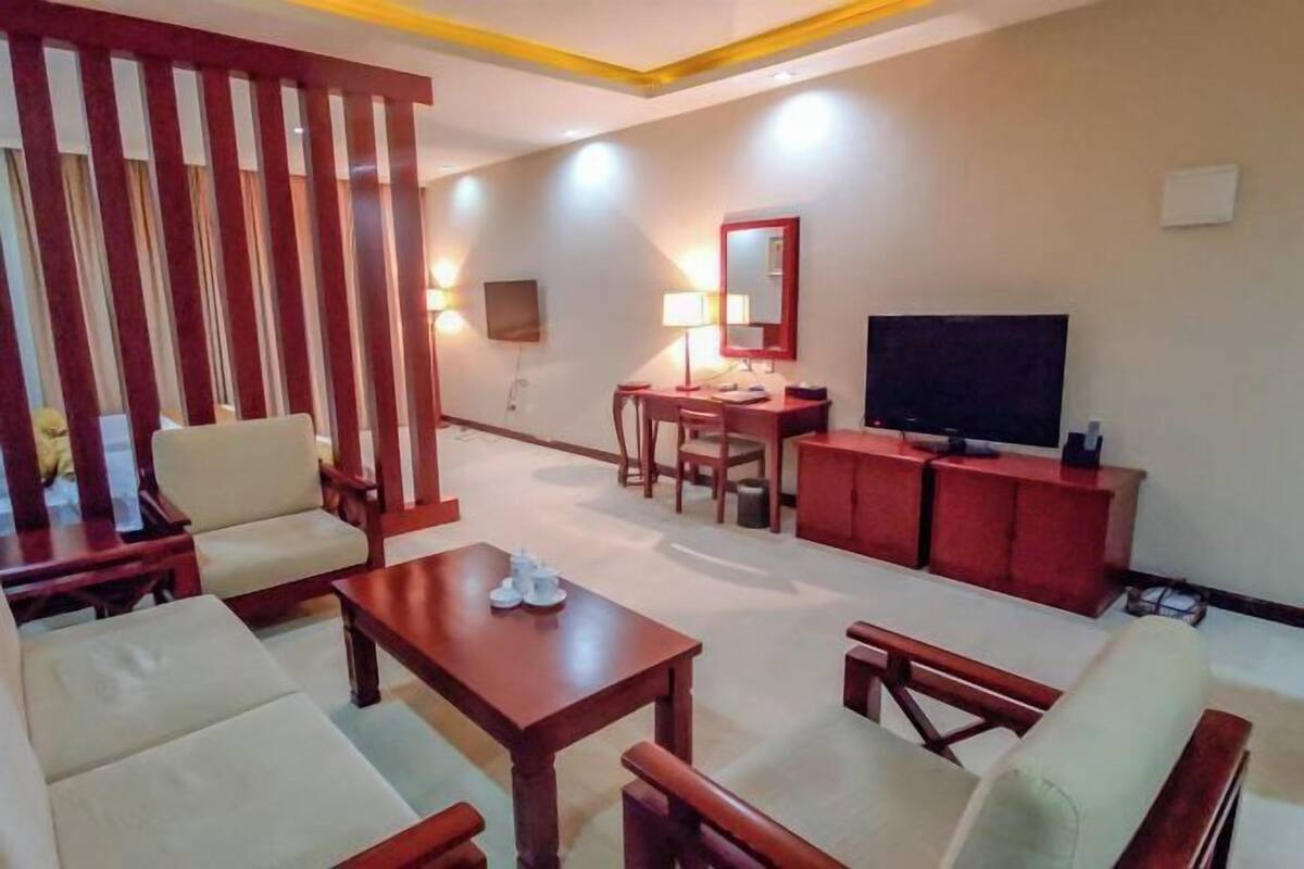 Una sala de estar con sofá, sillones, una mesa de centro, televisor y una mesita de noche con lámpara.