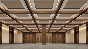 Un lobby moderno y espacioso de hotel con techo alto, paneles de madera y una columna central.