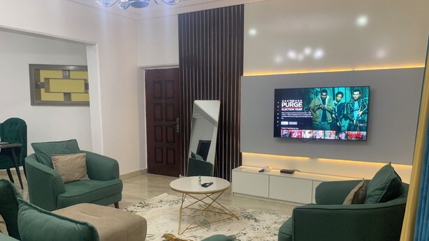 Una sala de estar moderna con sofás verdes, una mesa de centro y un televisor de pantalla plana montado en la pared.