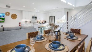 Une cuisine moderne avec des meubles blancs, un réfrigérateur en acier inoxydable et un coin repas doté d’une table en bois, mise pour quatre personnes.