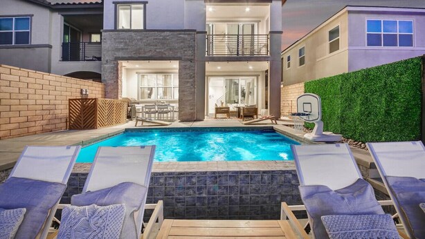 Une maison à deux étages avec une piscine, des chaises longues et un panier de basketball.
