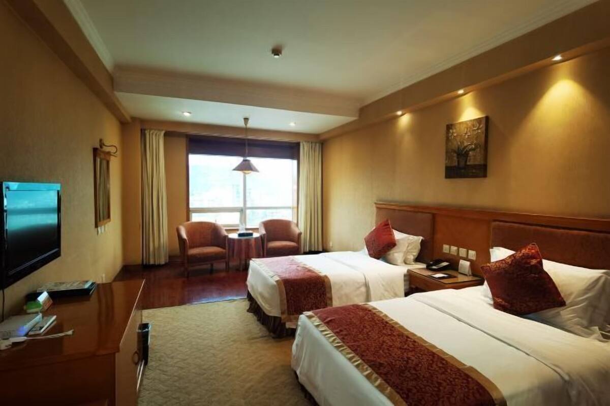 A hotel room with two beds, a desk, a TV, and a window with curtains.