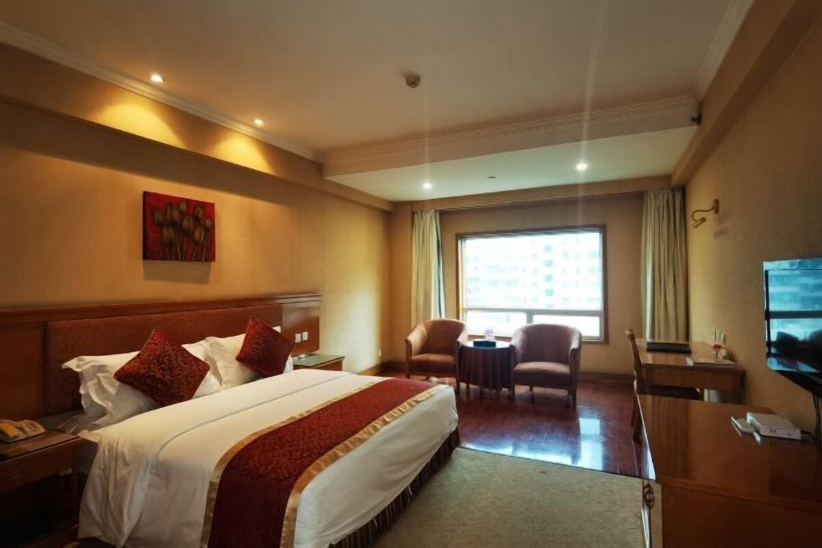 A hotel room with a large bed, a desk, a chair, and a TV.