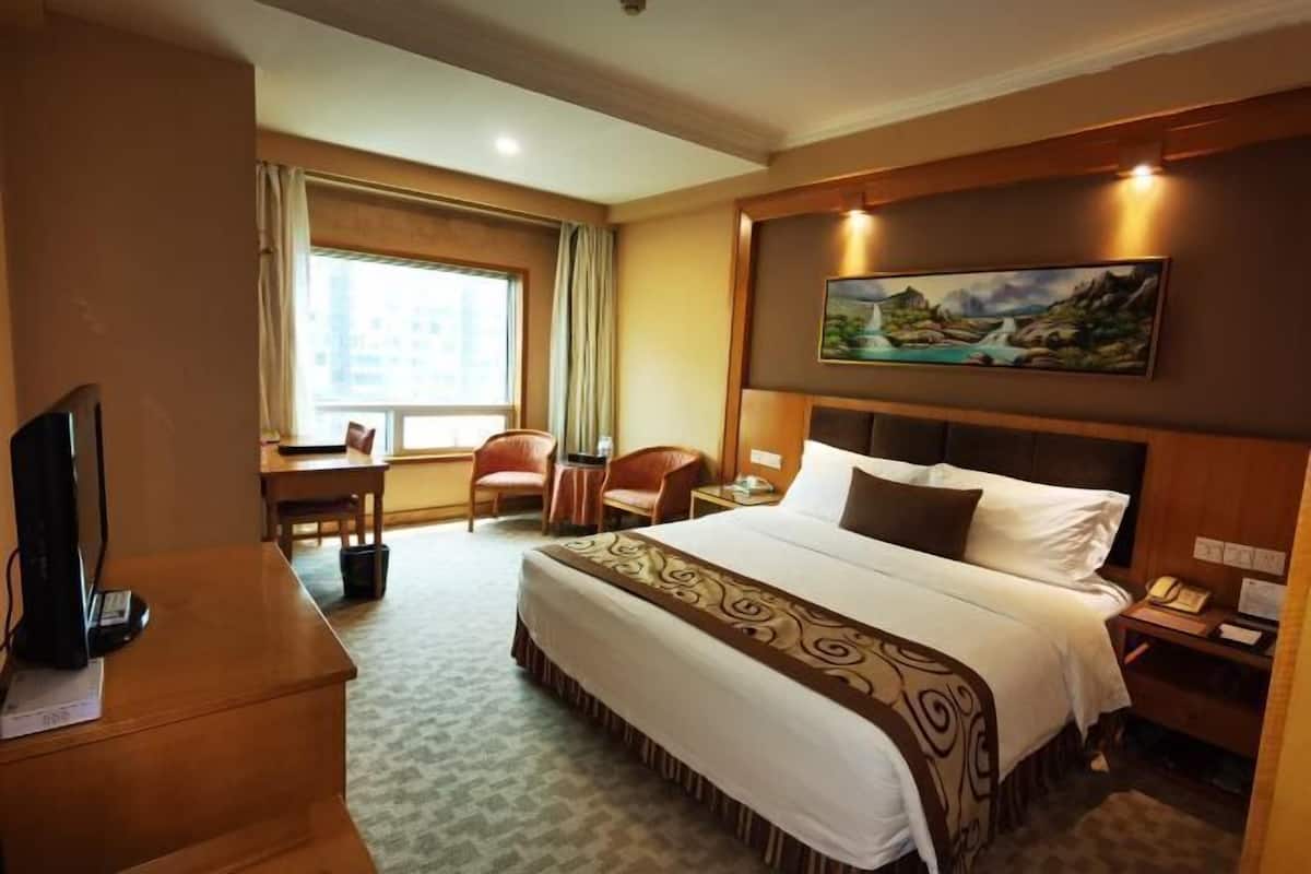 A hotel room with a large bed, a desk, a chair, a television, and a painting on the wall.