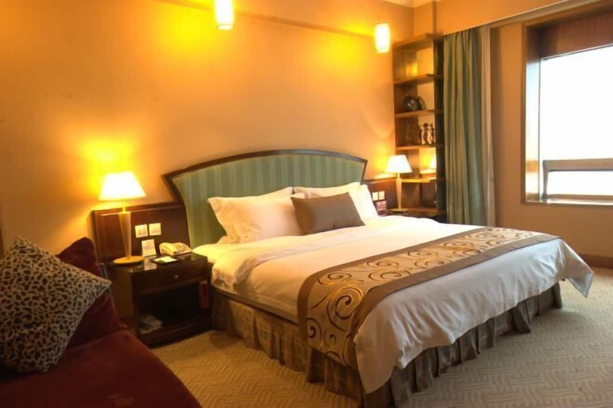 A hotel room with a large bed, two bedside tables with lamps, a red armchair, and a window with curtains.