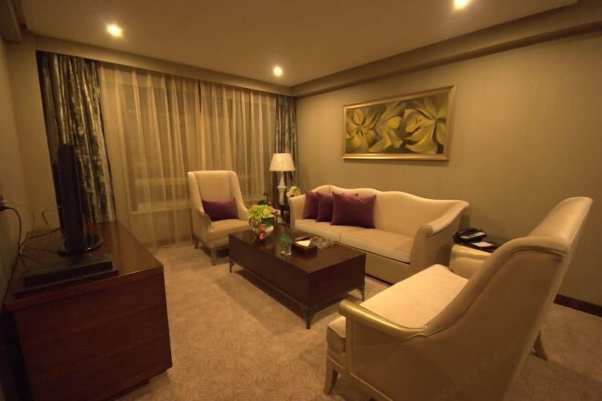 Quarto de hotel com sofá, poltronas, mesa de centro, escrivaninha e um quadro na parede.