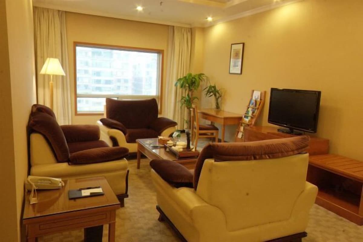 Quarto de hotel com sofás, televisão, escrivaninha e janela com cortinas.