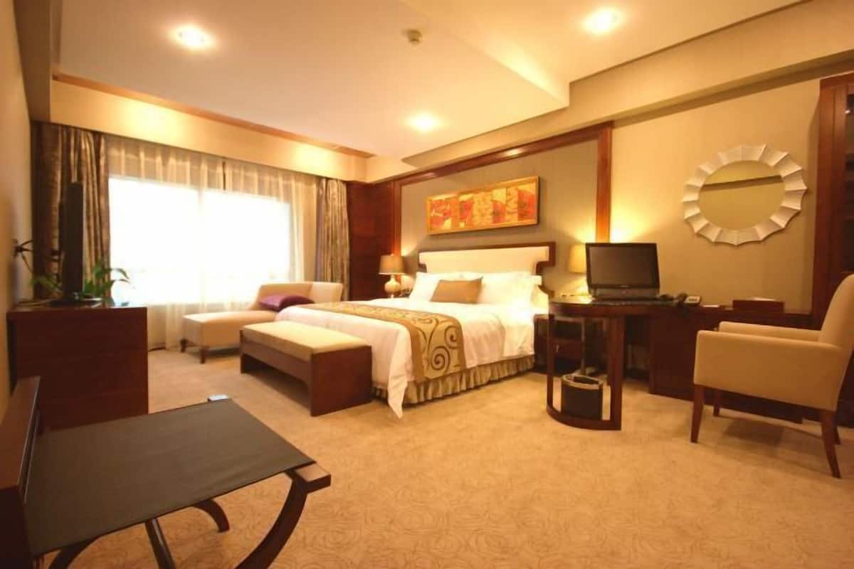 A hotel room with a bed, a desk, a chair, a TV, and a large window with curtains.