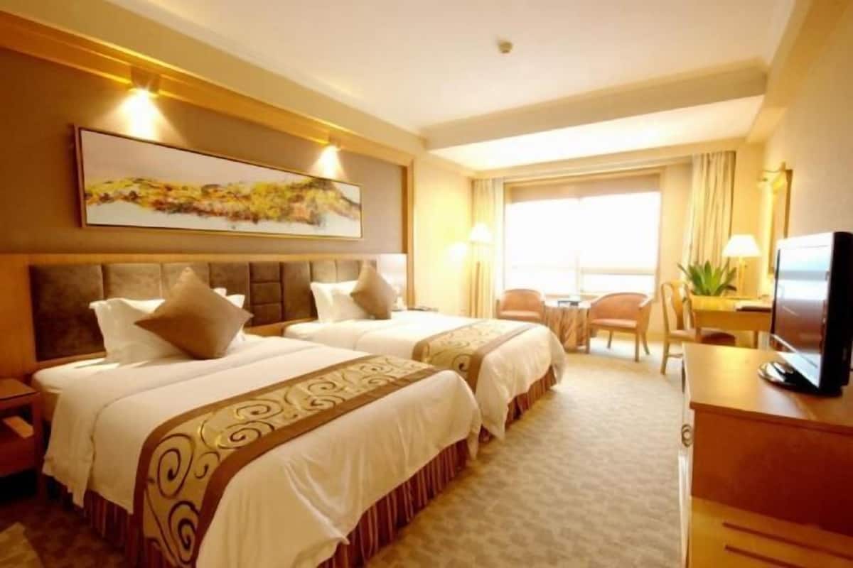 A hotel room with two beds, a desk, a television, and a large window.