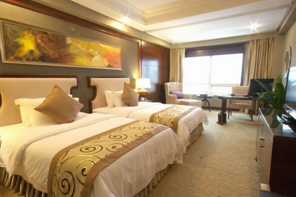A hotel room with two beds, a desk, a chair, a TV, and a large window.