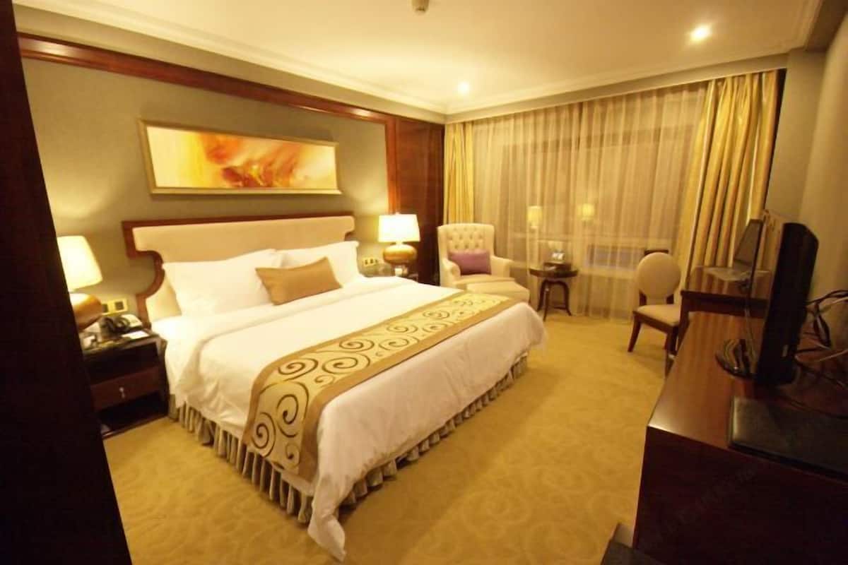 A hotel room with a large bed, a desk, a chair, a TV, and a painting on the wall.
