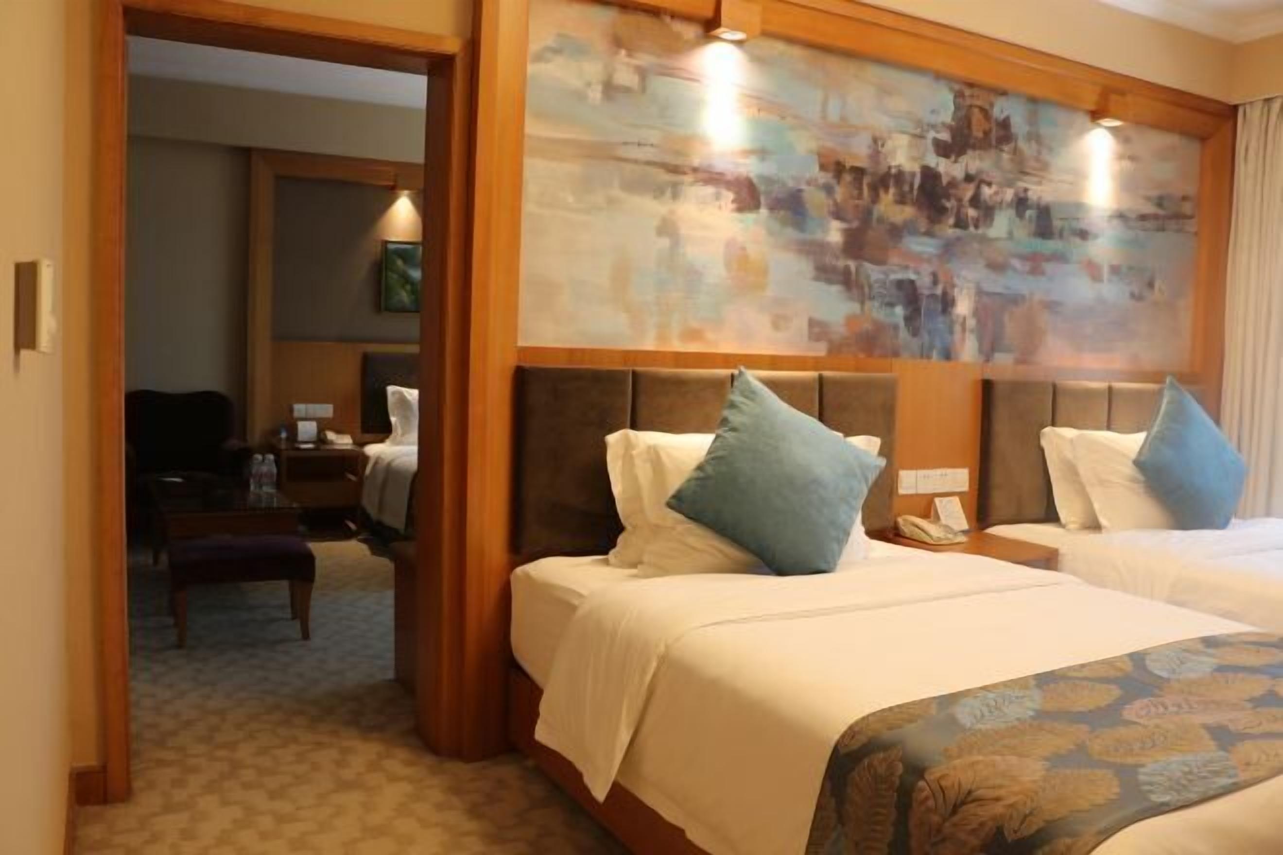 A hotel room with two beds, a wooden headboard, a painting above the beds, and a small desk with a telephone.