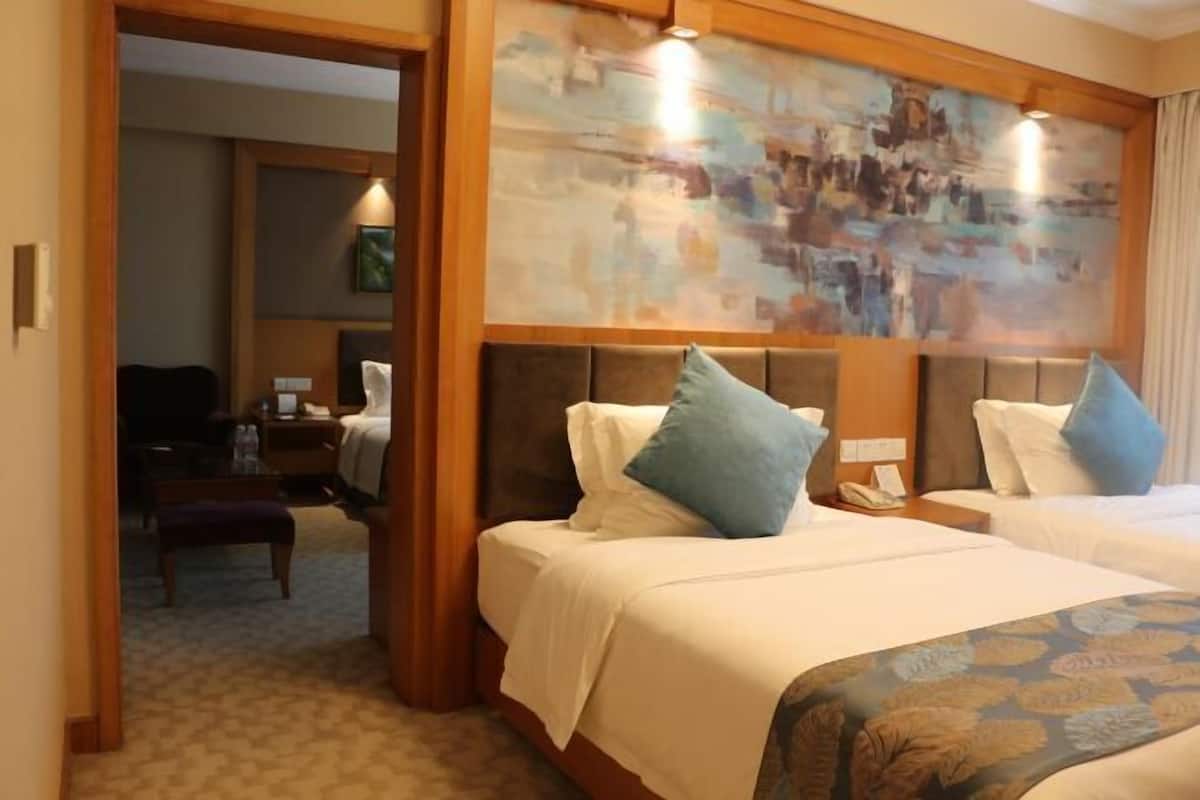 A hotel room with two beds, a wooden headboard, a painting above the beds, and a small desk with a telephone.
