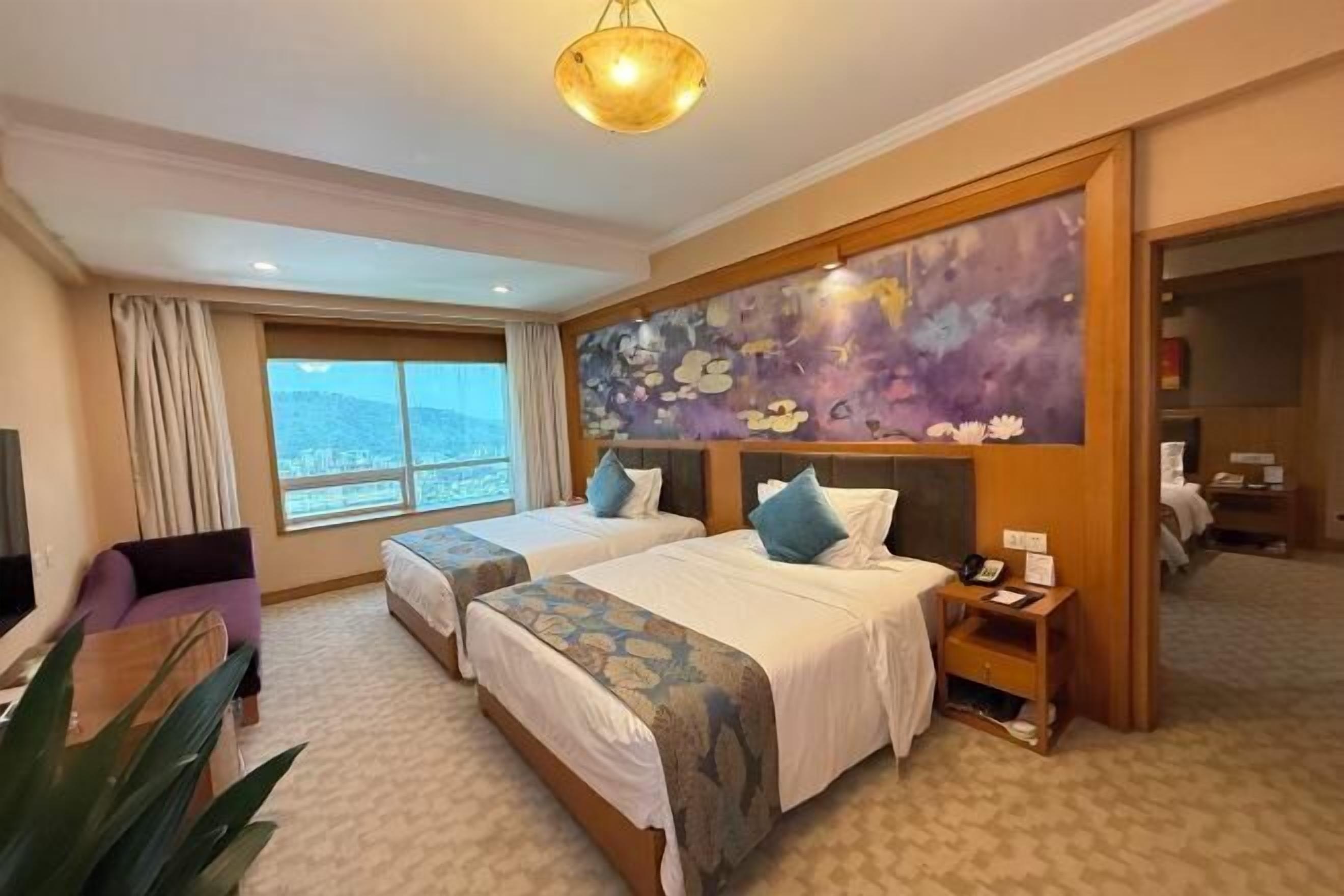 A hotel room with two beds, a large window, a painting on the wall, and a plant.